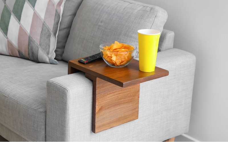 A DIY, wooden couch sleeve holding orange juice, chips and the tv remote