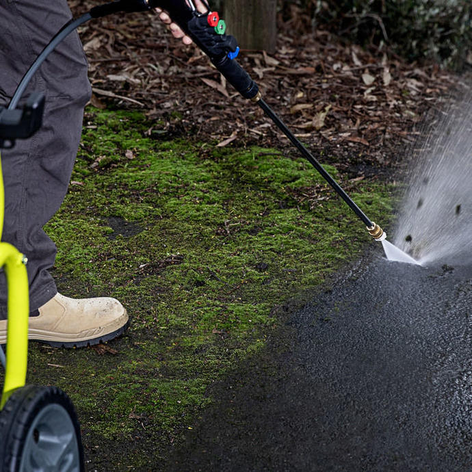 A Ryobi pressure washer being used to remove moss from dark concrete